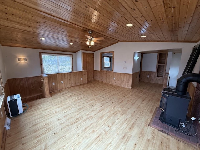 unfurnished living room with wood finished floors, lofted ceiling, a wood stove, wainscoting, and wooden ceiling