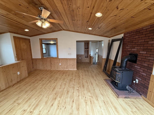 unfurnished living room featuring a wood stove, vaulted ceiling, hardwood / wood-style flooring, wood ceiling, and wainscoting