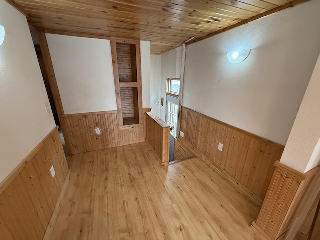 empty room with a wainscoted wall, wooden ceiling, light wood-style floors, and wooden walls