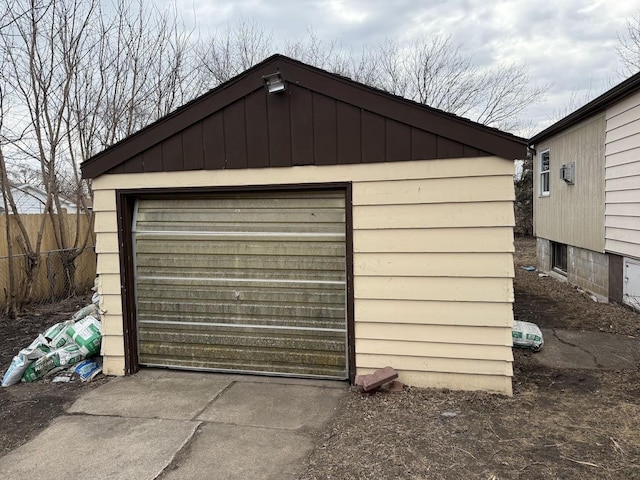 detached garage featuring concrete driveway and fence