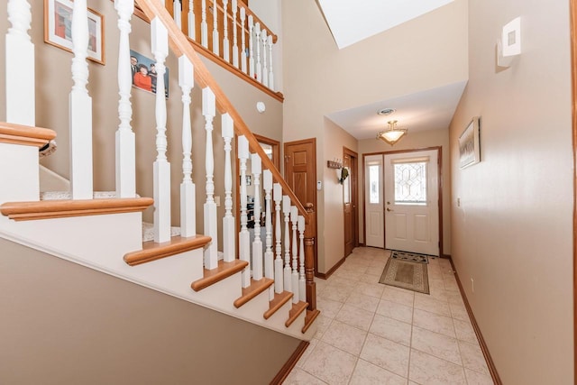 foyer entrance featuring tile patterned floors, baseboards, a towering ceiling, and stairs