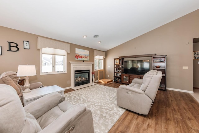 living area with a glass covered fireplace, baseboards, wood finished floors, and vaulted ceiling