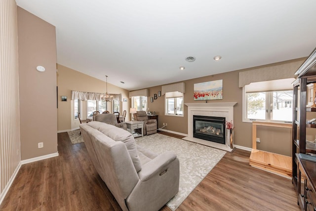 living area featuring wood finished floors, baseboards, lofted ceiling, a chandelier, and a tile fireplace