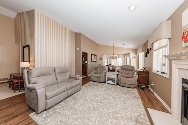 living area with lofted ceiling, an inviting chandelier, wood finished floors, and a tiled fireplace