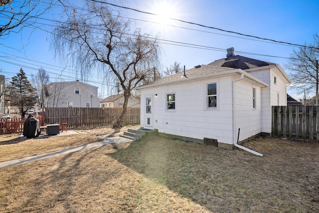 back of property with a yard, a chimney, and a fenced backyard