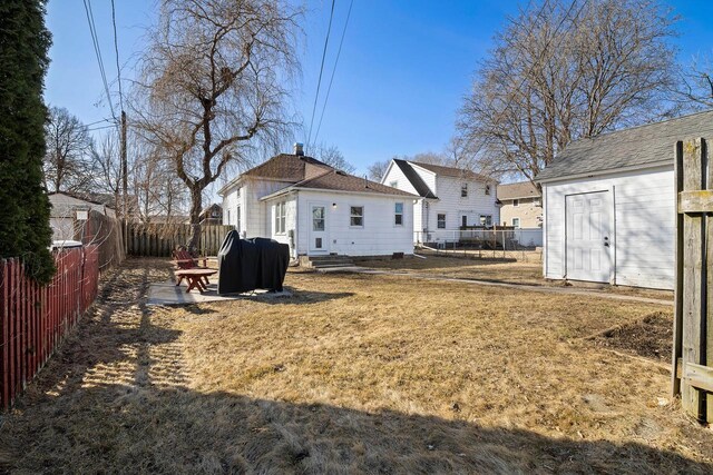 back of house featuring a fenced backyard, a lawn, entry steps, and an outdoor structure