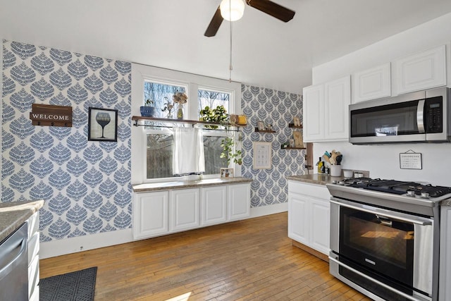 kitchen with baseboards, light wood finished floors, wallpapered walls, stainless steel appliances, and white cabinetry