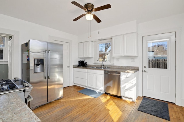 kitchen featuring light wood-type flooring, appliances with stainless steel finishes, white cabinets, a ceiling fan, and a sink