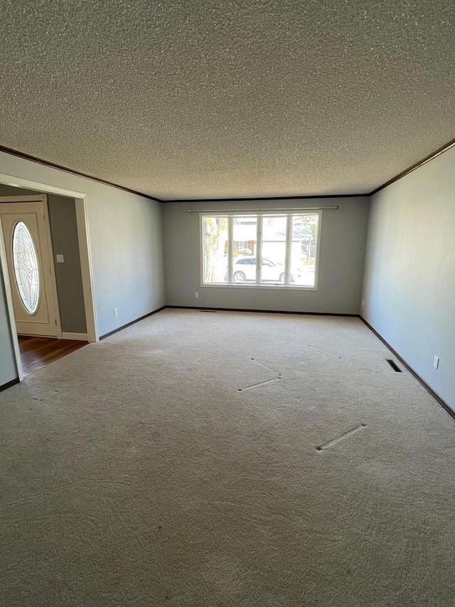 unfurnished living room with visible vents, crown molding, baseboards, carpet, and a textured ceiling