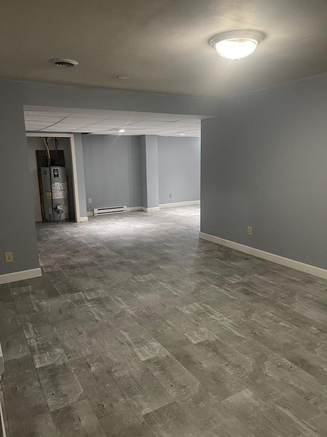 finished below grade area with baseboards, visible vents, dark wood-style flooring, gas water heater, and baseboard heating