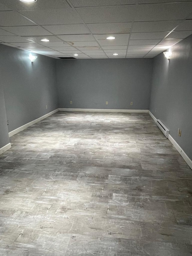 finished basement with a drop ceiling, wood finished floors, baseboards, and a baseboard radiator