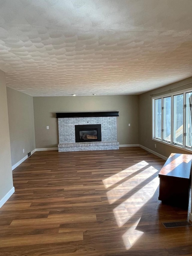 unfurnished living room featuring visible vents, dark wood-type flooring, baseboards, a fireplace, and a textured ceiling