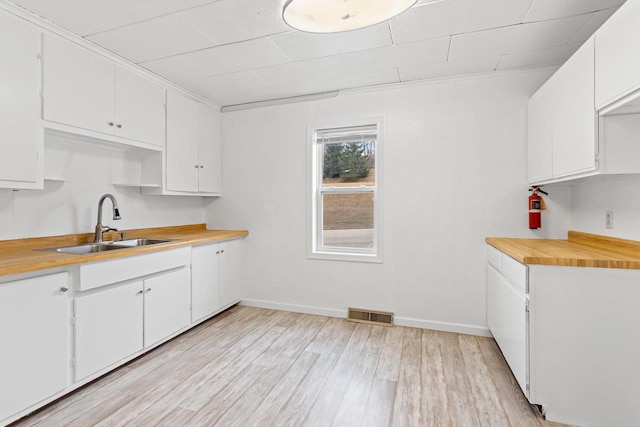 kitchen with visible vents, baseboards, light wood-style flooring, white cabinets, and a sink