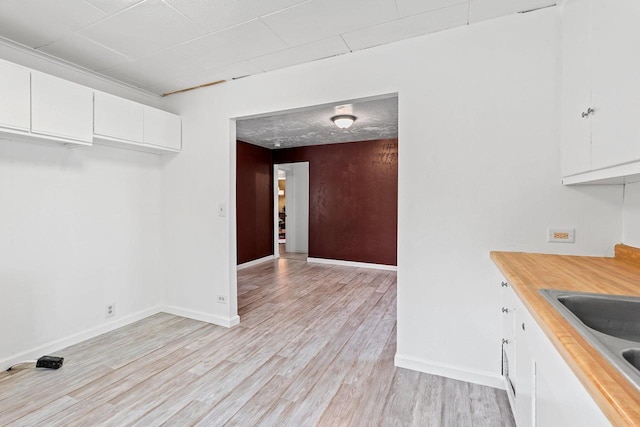 kitchen with baseboards, white cabinetry, light wood-style floors, and a sink