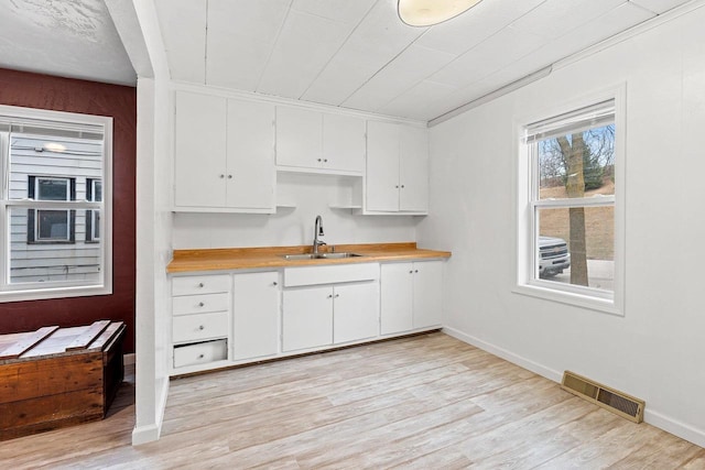 kitchen featuring visible vents, light wood finished floors, a sink, light countertops, and white cabinetry