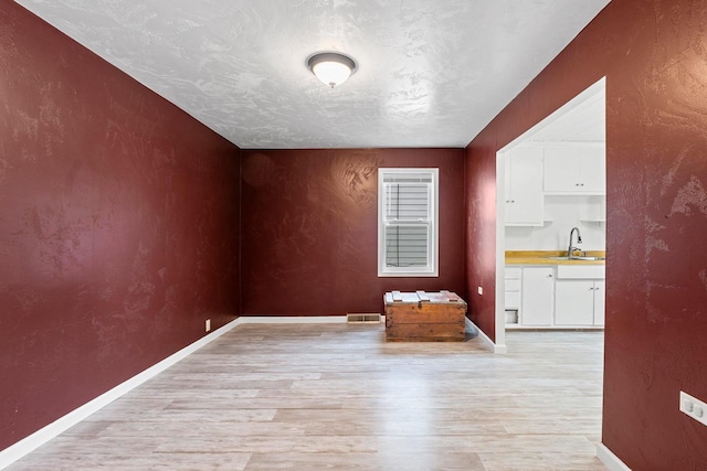 unfurnished dining area featuring light wood-type flooring, visible vents, a textured wall, and a sink