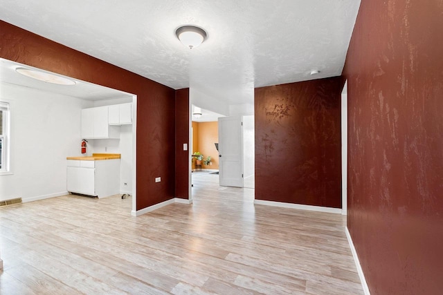 interior space with a textured ceiling, visible vents, light wood-type flooring, and baseboards