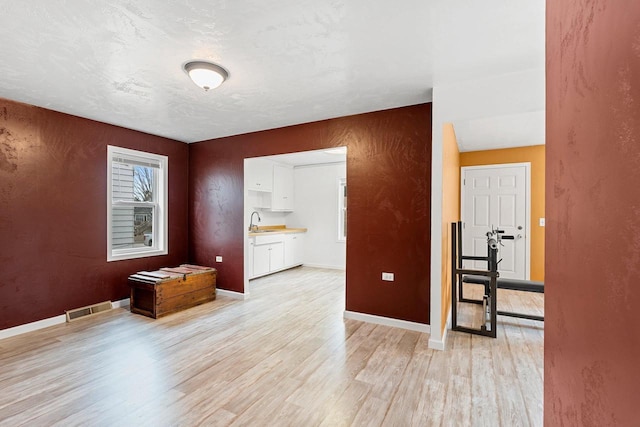 spare room featuring light wood finished floors, visible vents, baseboards, and a sink