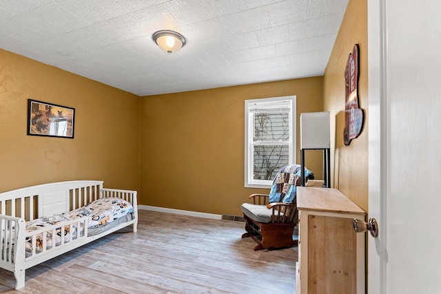 bedroom featuring a nursery area, wood finished floors, and baseboards