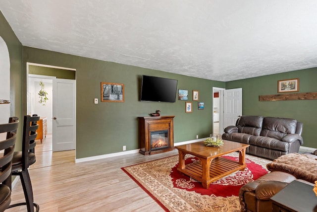 living room featuring baseboards, light wood-style floors, a glass covered fireplace, and a textured ceiling