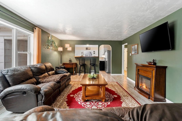 living area with baseboards, arched walkways, a glass covered fireplace, and light wood finished floors