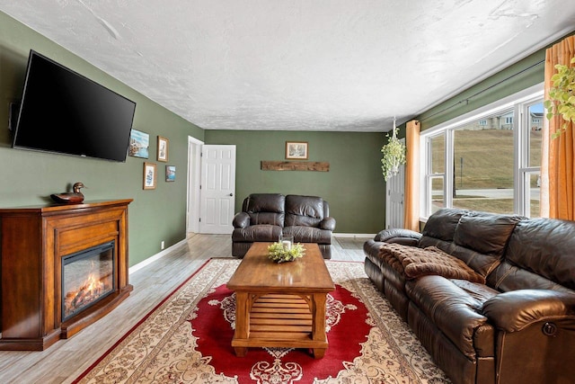 living room with baseboards, light wood-style floors, a glass covered fireplace, and a textured ceiling