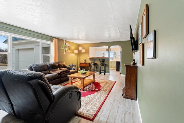 living area featuring baseboards, arched walkways, light wood-style floors, and a textured ceiling