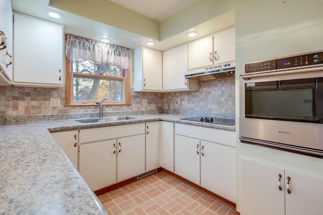 kitchen featuring a sink, oven, under cabinet range hood, black electric cooktop, and tasteful backsplash