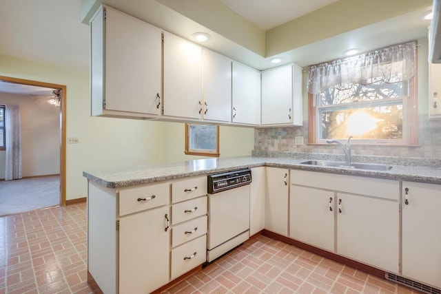 kitchen featuring a sink, backsplash, a peninsula, brick floor, and dishwasher