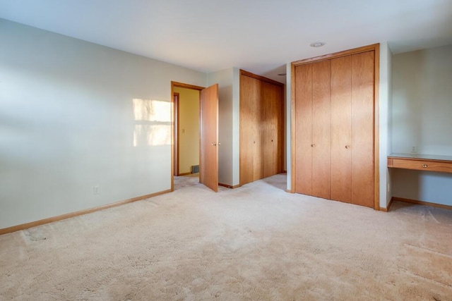 unfurnished bedroom featuring baseboards, carpet floors, and two closets