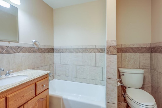 bathroom featuring tile walls, a wainscoted wall, toilet, a bathtub, and vanity