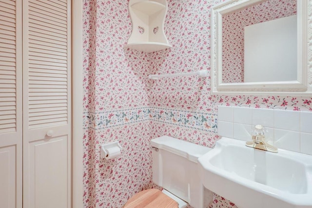 bathroom featuring a closet, wallpapered walls, toilet, and a sink