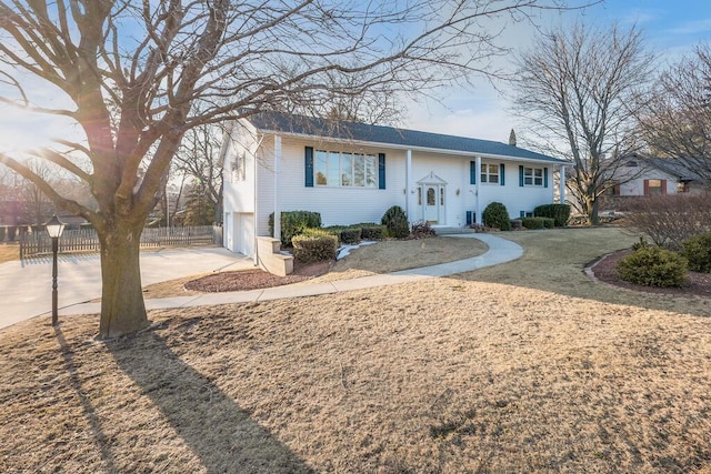 raised ranch featuring an attached garage, concrete driveway, and fence