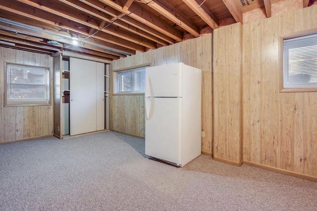 basement featuring wooden walls, freestanding refrigerator, and carpet floors