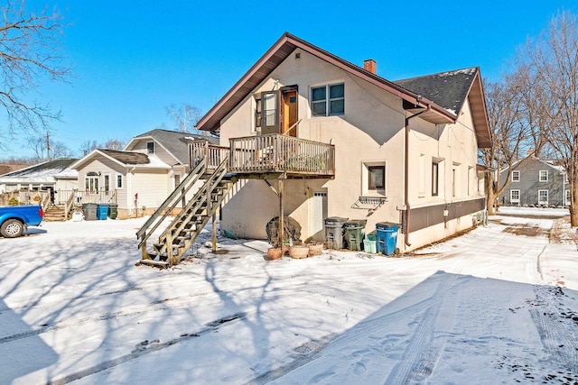 snow covered property featuring stairway, stucco siding, and a chimney