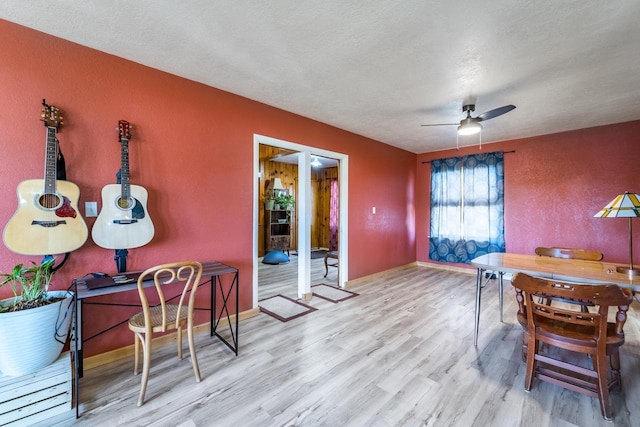 dining space featuring a textured ceiling, wood finished floors, baseboards, ceiling fan, and a textured wall