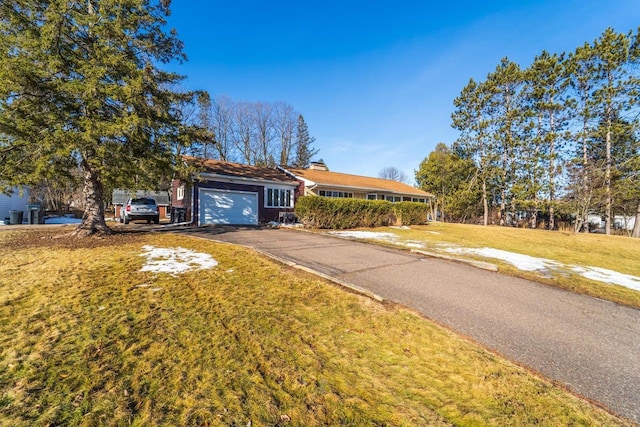 ranch-style home featuring driveway, a chimney, a garage, and a front yard