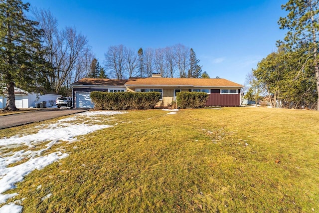 single story home featuring aphalt driveway, an attached garage, a chimney, and a front lawn