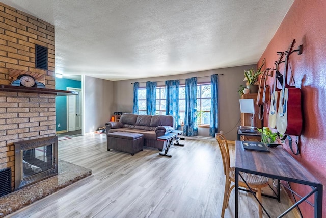 living area featuring a fireplace, a textured ceiling, baseboards, and wood finished floors