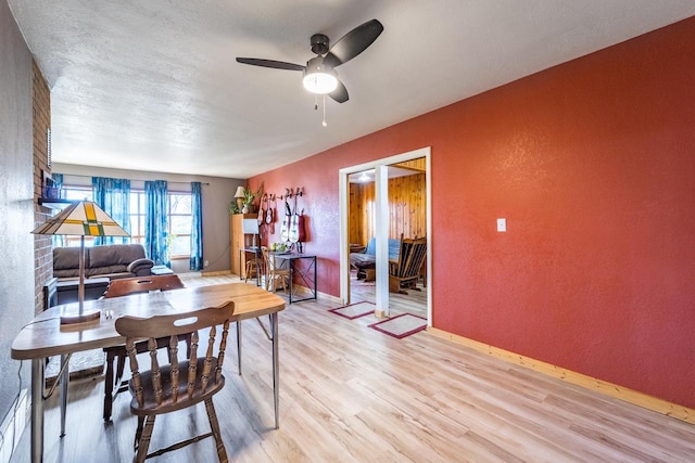 dining room with a textured wall, baseboards, light wood finished floors, and ceiling fan