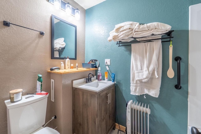 bathroom featuring vanity, radiator, toilet, and a textured wall