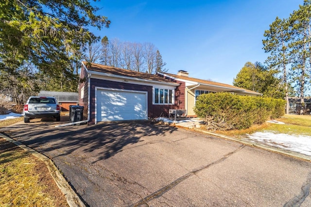 ranch-style house featuring aphalt driveway, a chimney, a garage, and fence