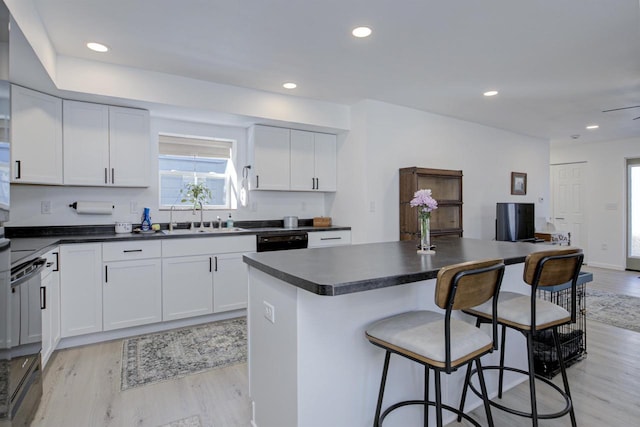 kitchen featuring dark countertops, a kitchen breakfast bar, light wood-style flooring, and a sink