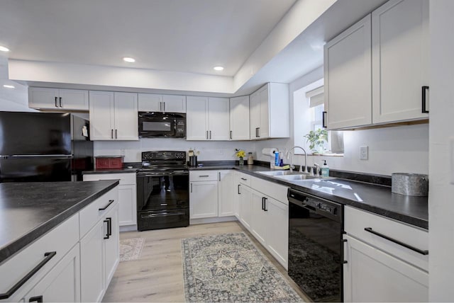 kitchen featuring black appliances, a sink, dark countertops, recessed lighting, and light wood-style floors