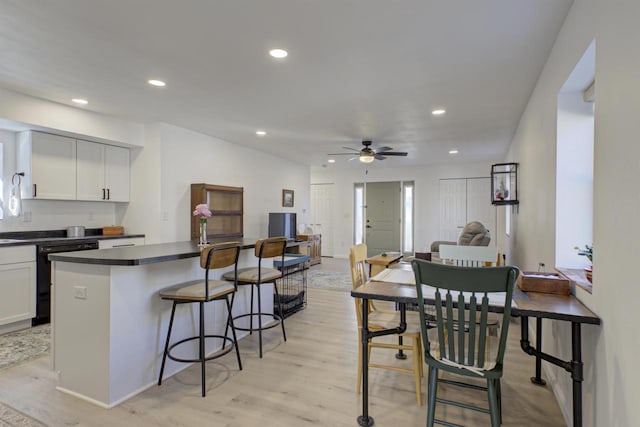 kitchen featuring dishwashing machine, light wood-style flooring, recessed lighting, dark countertops, and a kitchen breakfast bar