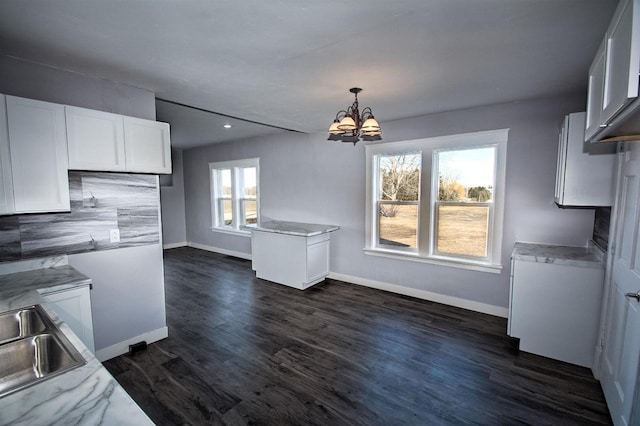 kitchen with baseboards, dark wood finished floors, an inviting chandelier, white cabinetry, and a sink