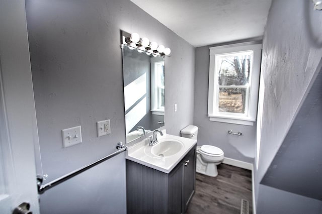 half bathroom with vanity, toilet, wood finished floors, and baseboards