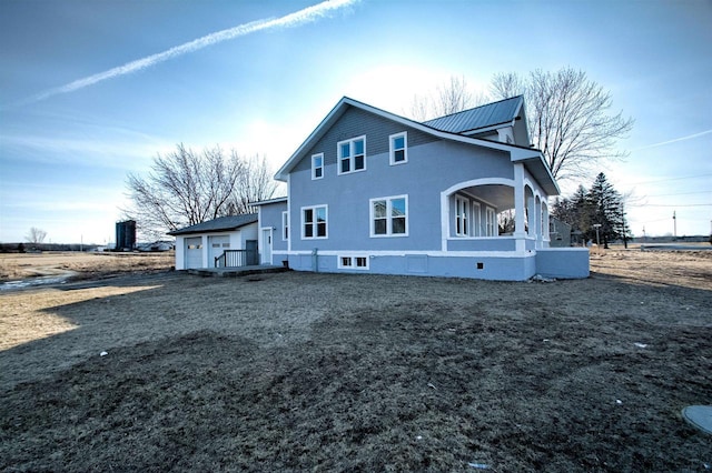 back of house with stucco siding, a garage, and metal roof