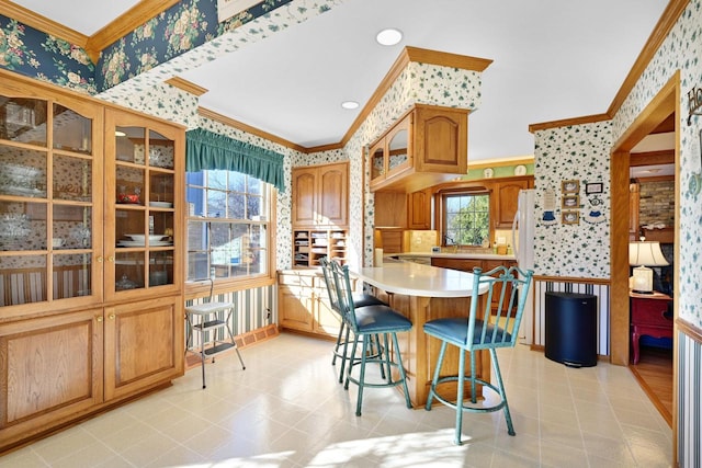 kitchen featuring wallpapered walls, glass insert cabinets, a breakfast bar, light countertops, and ornamental molding