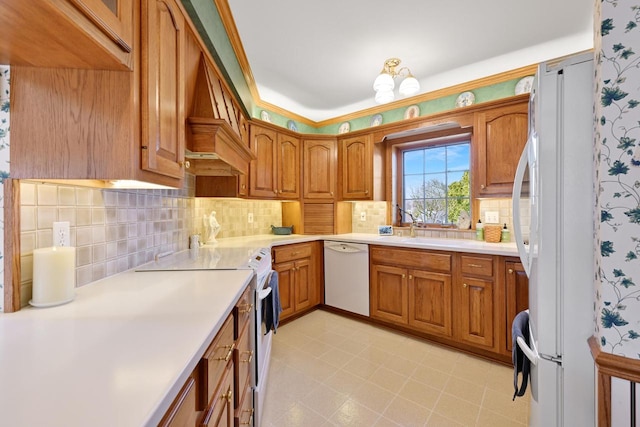 kitchen featuring white appliances, light countertops, brown cabinets, and a sink